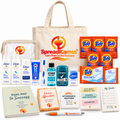 A comprehensive self-care and productivity gift set from SpreadKarma, featuring a beige tote bag, a clear zippered toiletry case, three Dove body wash bottles, a tube of toothpaste, a Listerine bottle, a Degrum mouthwash bottle, Qlips mouthwash, Tide laundry detergent, dryer sheets, sticky notes, affirmation cards, a road map, and a pen.